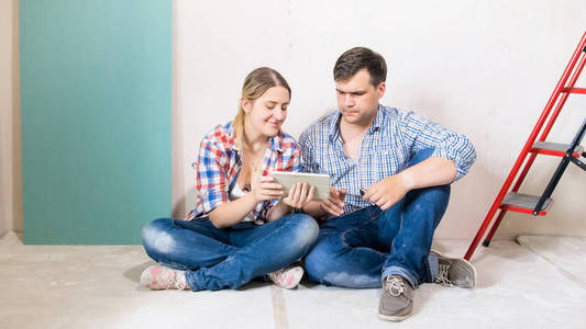 快乐的年轻夫妇坐在地板上的建筑和使用数码片
