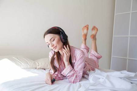 穿粉红色睡衣的黑发在床上听音乐与耳机