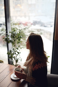 微笑的妇女穿着毛衣和围巾在咖啡馆与杯咖啡