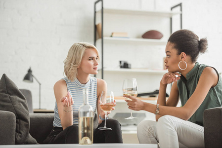 多民族年轻妇女坐在一起, 用白葡萄酒酒杯交谈