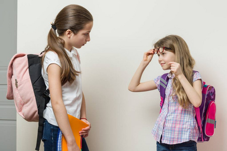 两个女孩在学校的沟通。学生背包, 背景明亮的墙壁在学校