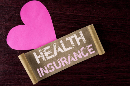 概念性手写显示健康保险。商业照片展示健康保险信息覆盖医疗服务提供商写在折叠纸板纸上的木质背景心脏