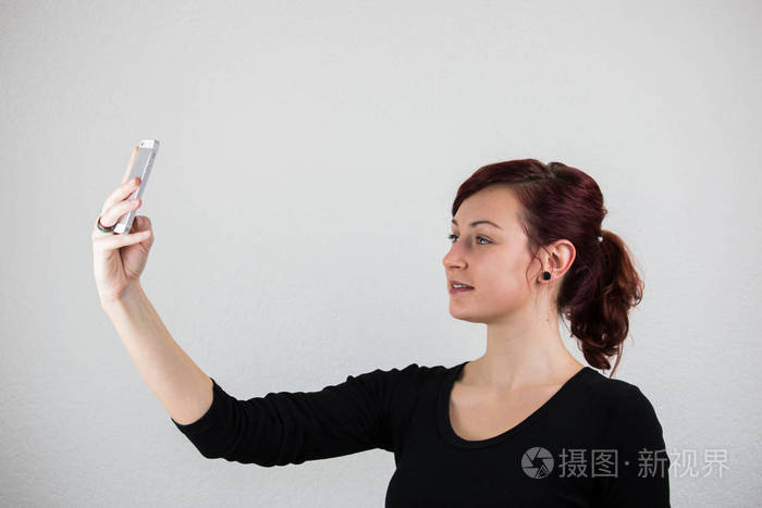 一个年轻的女孩用手机拿着一个前摄像头, 一个白色的 b照片-正版商用