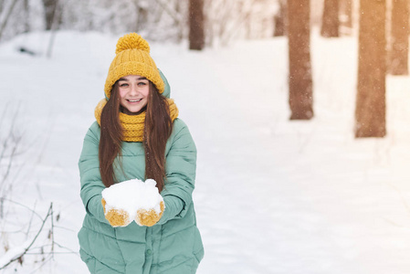 一个美丽的女孩戴着一顶针织帽子, 手里拿着雪, 在冬天森林的背景下。