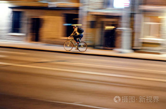 运动模糊.夜间城市景观中男性骑自行车的模糊图像, 速度概念照片-正版