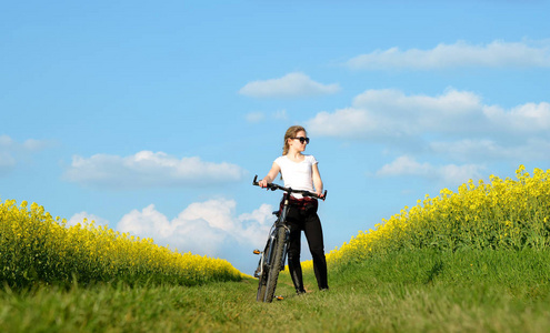 骑自行车的女孩在油菜地里的泥土路上。健康的生活方式概念