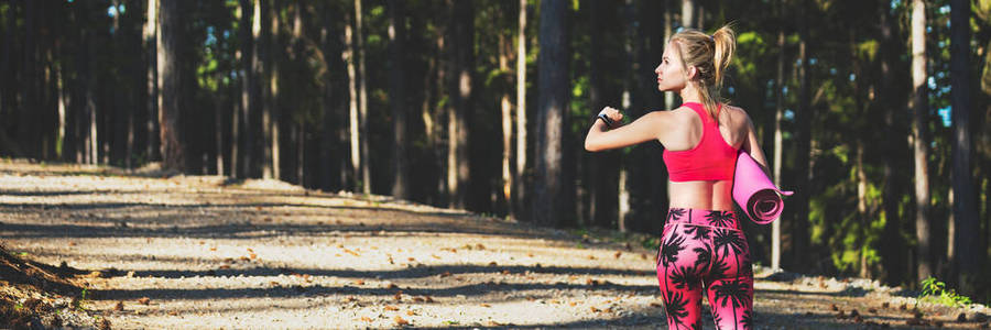 年轻的健身运动妇女穿着智能手表, 拿着瑜伽垫, 从相机里走开。精神和身体网络横幅