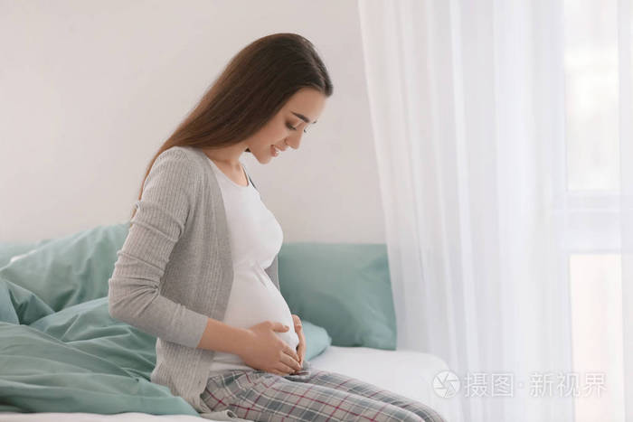 早晨坐在床上的美丽的孕妇