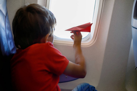 小家伙玩红色纸飞机，在飞机飞行过程中的男孩