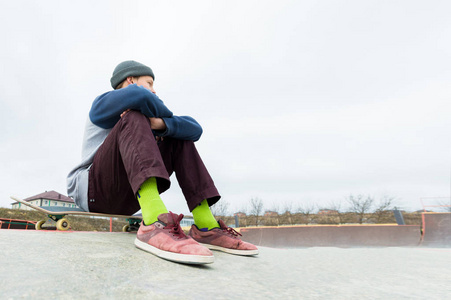 一个十几岁的男孩坐在公园的滑板上。城市青少年闲暇消遣的概念