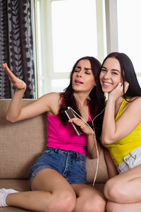 特写照片两个微笑的年轻妇女与耳机听音乐从手机在家里的沙发上