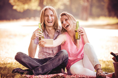 快乐的情侣在野餐时用智能手机制作自拍。微笑的白种情侣在草地上的乐趣, 并采取自拍