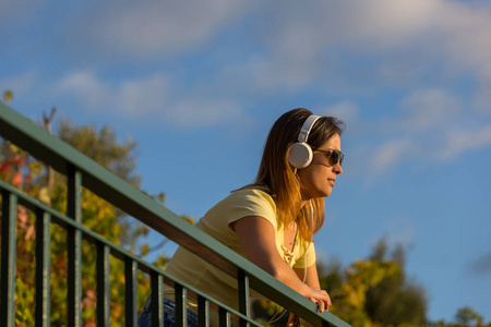 在日落的女人享受音乐, 用耳机, 户外