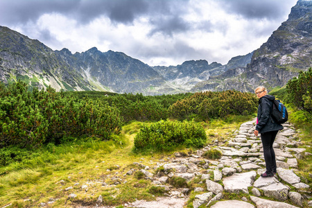 徒步旅行的妇女在山路远足与背包, 路与石头在高山, 全景风景