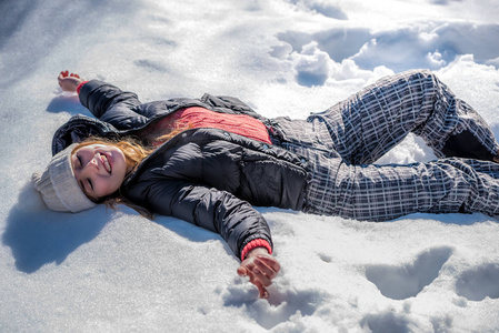 年轻可爱的女人躺在玩和享受冬天的雪