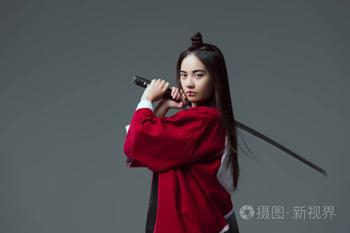 穿着和服的年轻女子手持武士刀, 看着相机在灰色隔离