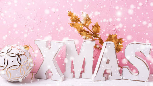 粉红色的圣诞节。词圣诞节由木信件, 球和金黄分支在白色木质背景反对粉红色墙壁。绘制的雪