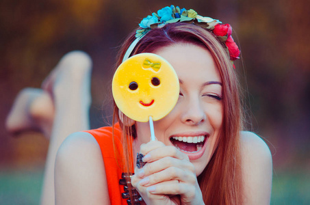 红头发的女孩玩黄色 emoji 表情糖果在棍子上