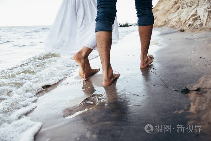 一对相爱的情侣赤脚走在沙滩上的湿沙上