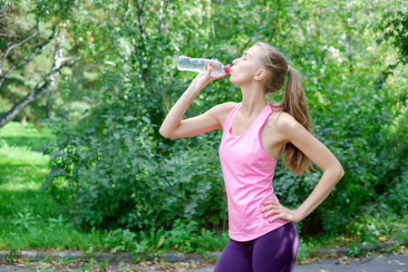 运动的年轻妇女从瓶子里喝水。户外运动