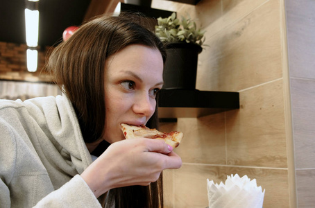 黑发年轻饥饿的妇女咬掉美味的比萨饼和吃它, 侧面视图