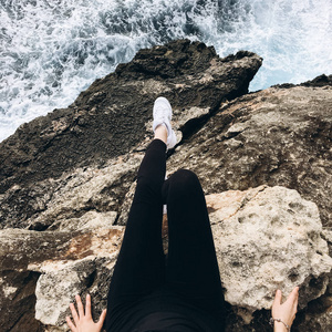 在海岸岩石山的白色运动的鞋子女性腿的看法