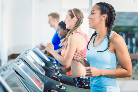 一个适合快乐的女人和她的训练小组在健身房跑步机的侧面视图