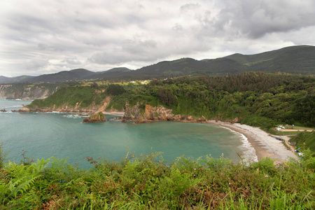 海海湾与陡峭的海岸的看法。乌云密布的天空, 远处有一道明亮的绿草和小山。西班牙北部的夏季日