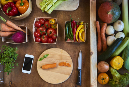 用菜刀和智能手机在乡下的切板上切胡萝卜。美味素食烹饪配料