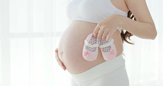 怀孕妇女站立和举行小婴儿鞋