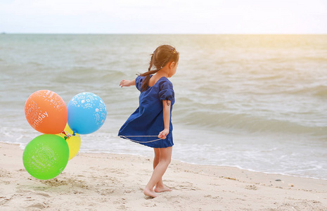 可爱的小女孩玩气球与文本 生日快乐 在海滩上