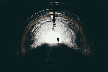 黑暗的城市隧道里孤独的身影走向光明。走到光明的人