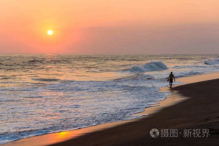 男性冲浪者在海滩上漫步日落的剪影