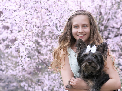 美丽的小女孩与狗在一棵开花的树的背景上