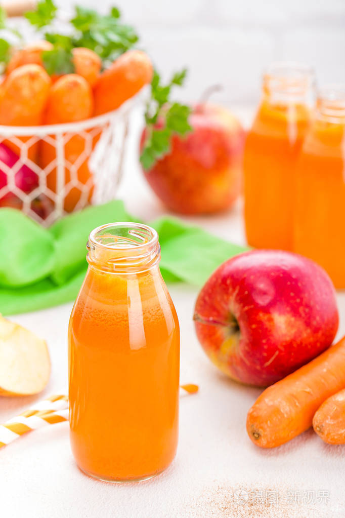 新鲜胡萝卜和苹果汁的白色背景.胡萝卜和苹果汁在玻璃瓶的白色桌上, 