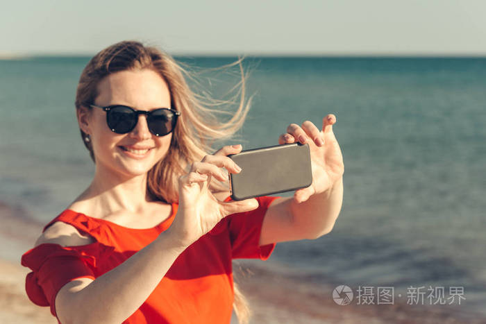 年轻漂亮的金发碧眼女人用在海滩上的手机