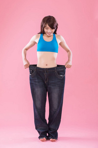 穿牛仔裤, 在粉红色的背景下显示体重下降的妇女