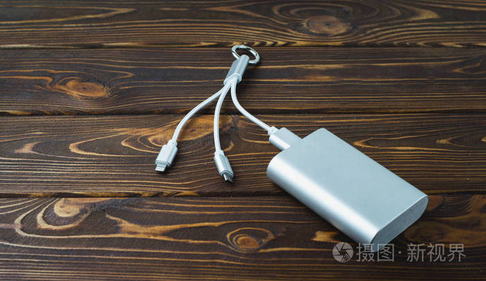 用灰色便携式外置电池 powerbank 在木桌上充电智能手机