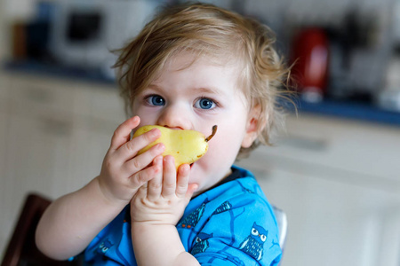 逗人喜爱的可爱的学步女孩吃新鲜的梨。饥饿快乐婴孩一年举行果子