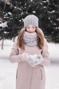 少女抱着心形的雪花球。年轻女孩在针织围巾, 手套和帽子站在冬季森林。冬天的心情。冬季时间