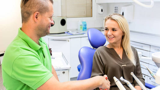 满意的微笑的妇女的画像在牙治疗以后握手与牙医