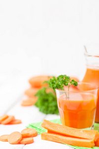 胡萝卜汁在美丽的眼镜, 切橙蔬菜和绿色欧芹的白色木质背景。鲜橙饮料。关闭摄影。选择性对焦。垂直横幅