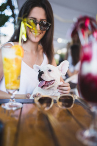 美丽的年轻女子与她的法国斗牛犬小狗在咖啡馆酒吧享受与太阳镜