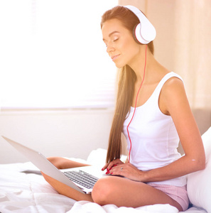 年轻漂亮的女人在床上听音乐