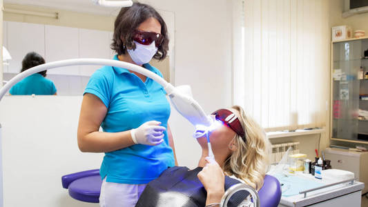 年轻的金发女人坐在牙医的椅子上牙齿美白程序