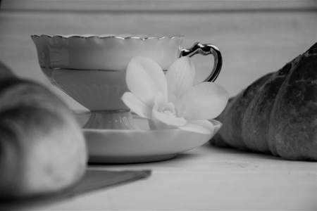 一个咖啡杯与热的浓咖啡, 牛角面包, 餐巾和兰花花在木质背景, 黑白相间