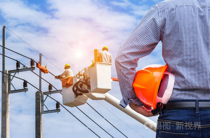 电气工程师在蓝天背景下用斗式液压升降平台在电力杆上工作的电工手持