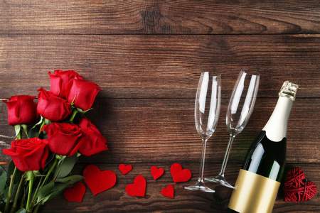 带眼镜的香槟瓶和木桌上的红玫瑰花