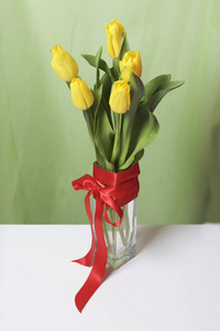 一束黄色的郁金香站在一个玻璃花瓶里, 裹着一只红丝带, 绑在弓上。