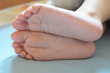 蓝色的床单两岁儿童脚的特写在浅蓝色床单上铺设照片